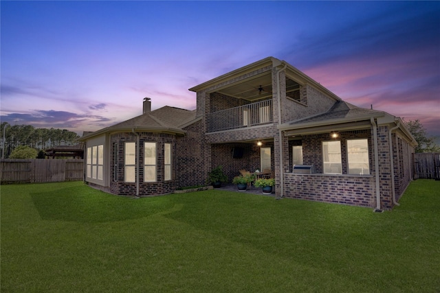 back house at dusk featuring a lawn, ceiling fan, and a balcony