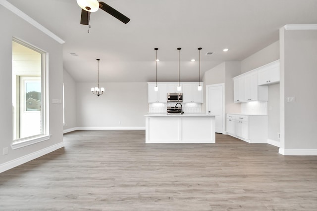 kitchen featuring a center island with sink, pendant lighting, white cabinetry, and backsplash