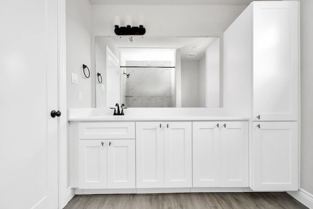 bathroom with a tile shower, vanity, and wood-type flooring