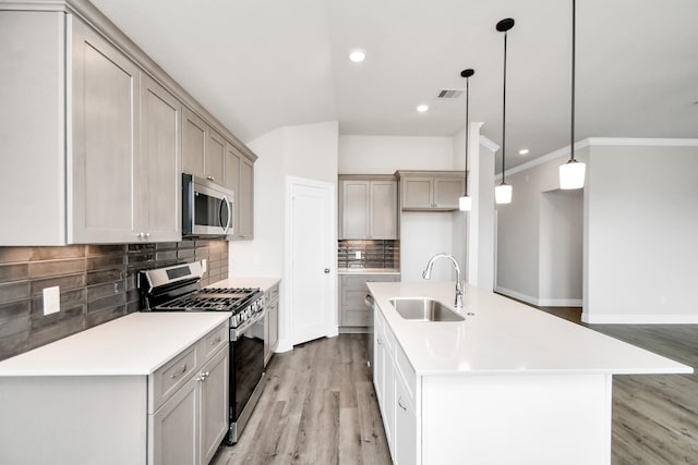 kitchen with decorative light fixtures, sink, stainless steel appliances, and a kitchen island with sink