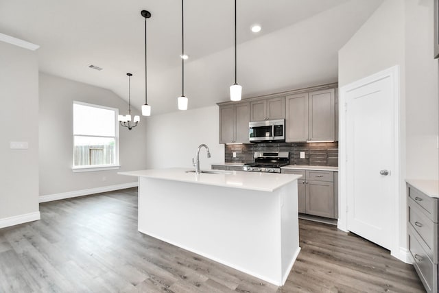 kitchen featuring appliances with stainless steel finishes, vaulted ceiling, a kitchen island with sink, pendant lighting, and dark hardwood / wood-style floors