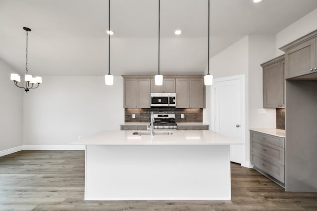 kitchen with stainless steel appliances, sink, dark hardwood / wood-style floors, hanging light fixtures, and an island with sink