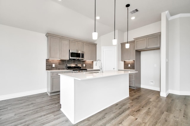 kitchen featuring sink, stainless steel appliances, light hardwood / wood-style flooring, backsplash, and a kitchen island with sink