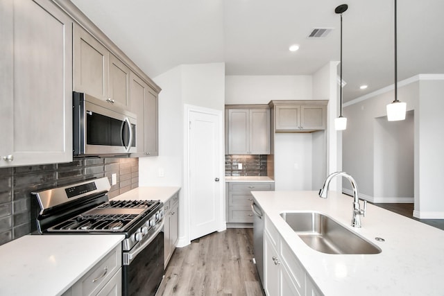 kitchen with appliances with stainless steel finishes, backsplash, sink, light hardwood / wood-style floors, and hanging light fixtures