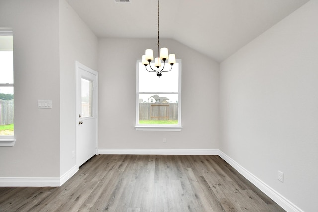 unfurnished dining area featuring light hardwood / wood-style flooring, a healthy amount of sunlight, lofted ceiling, and a notable chandelier