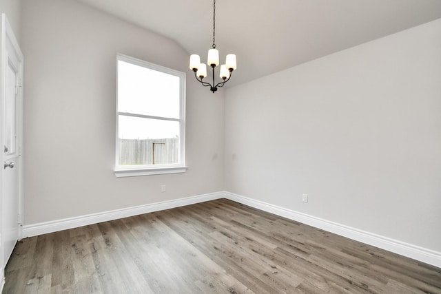 empty room with wood-type flooring, lofted ceiling, and an inviting chandelier