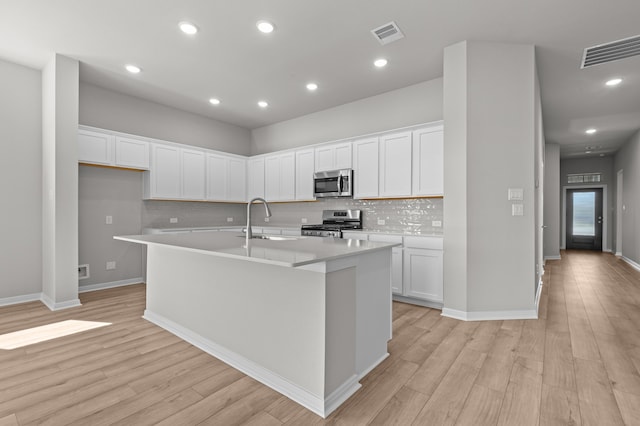 kitchen featuring an island with sink, light wood-type flooring, stainless steel appliances, and white cabinets