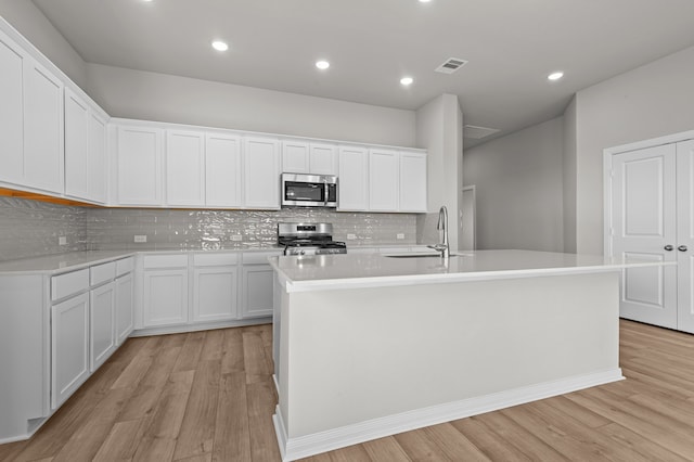 kitchen with a kitchen island with sink, stainless steel appliances, and white cabinets