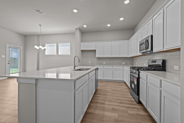 kitchen with light hardwood / wood-style floors, sink, an island with sink, appliances with stainless steel finishes, and white cabinetry