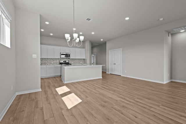 kitchen featuring a chandelier, light wood-type flooring, stainless steel appliances, an island with sink, and white cabinets