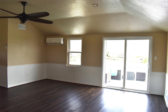 unfurnished room with lofted ceiling, dark wood-type flooring, a wall mounted air conditioner, and a textured ceiling