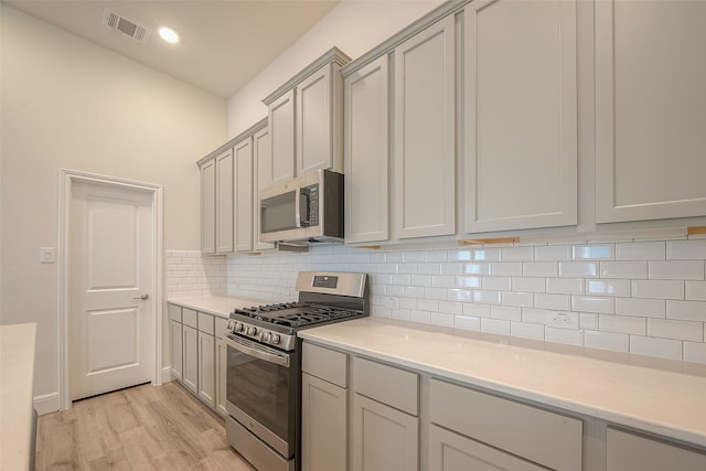 kitchen featuring gray cabinetry, decorative backsplash, light wood-type flooring, and appliances with stainless steel finishes