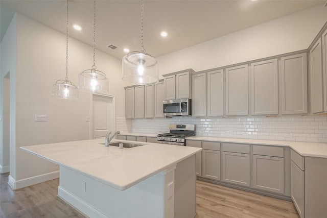 kitchen with light wood-type flooring, an island with sink, stainless steel appliances, and sink