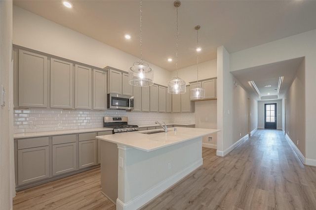 kitchen featuring sink, stainless steel appliances, light hardwood / wood-style floors, decorative backsplash, and a center island with sink