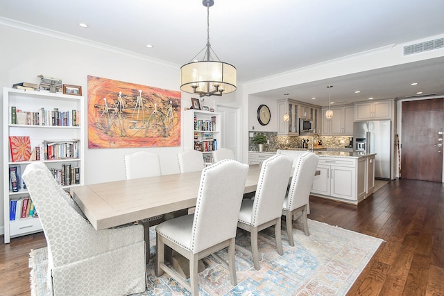 dining area featuring dark wood-type flooring, ornamental molding, and a notable chandelier