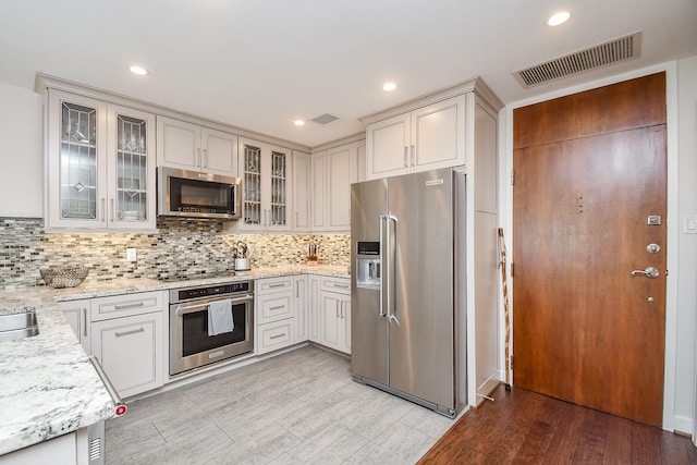 kitchen with stainless steel appliances, light stone counters, tasteful backsplash, and light hardwood / wood-style flooring