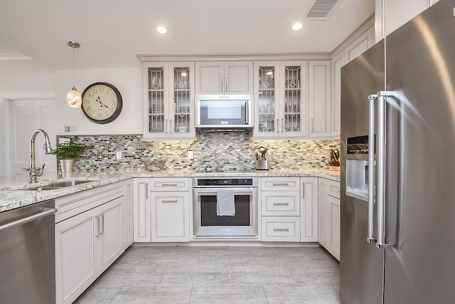 kitchen with sink, hanging light fixtures, decorative backsplash, light stone counters, and stainless steel appliances