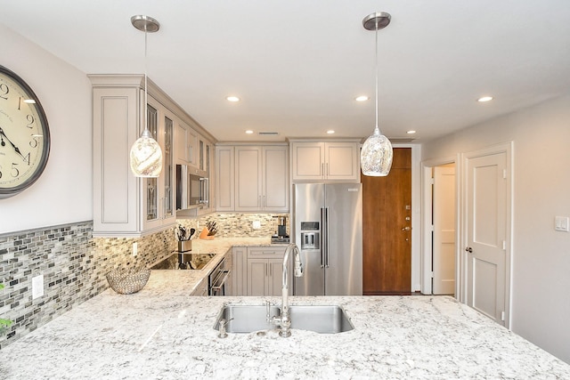 kitchen featuring tasteful backsplash, light stone counters, stainless steel appliances, sink, and decorative light fixtures