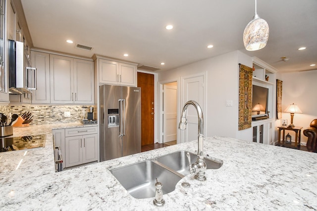 kitchen with sink, hanging light fixtures, decorative backsplash, light stone counters, and stainless steel appliances