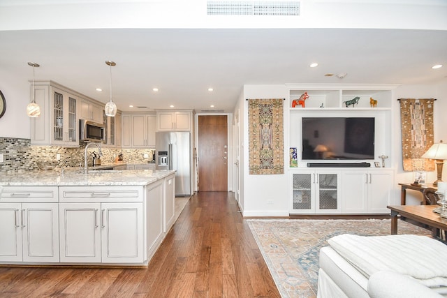 kitchen featuring decorative backsplash, appliances with stainless steel finishes, light wood-type flooring, light stone counters, and hanging light fixtures