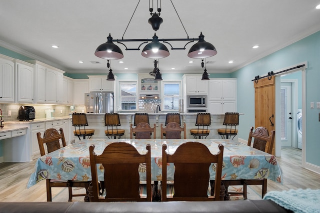 dining room featuring washer / dryer, a barn door, light wood-type flooring, and crown molding