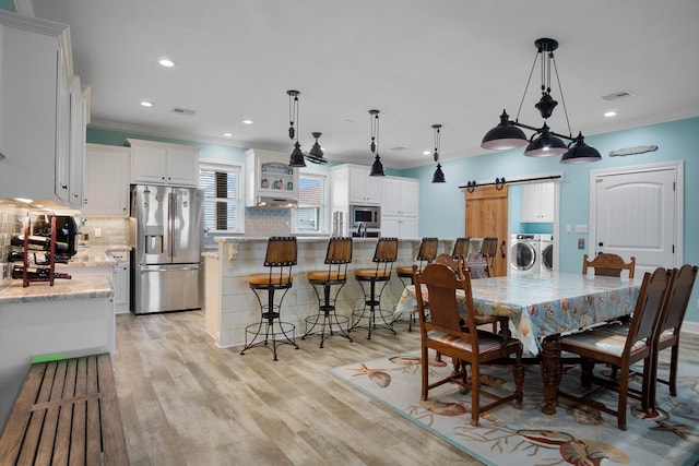 dining area featuring a barn door, light hardwood / wood-style floors, ornamental molding, and independent washer and dryer