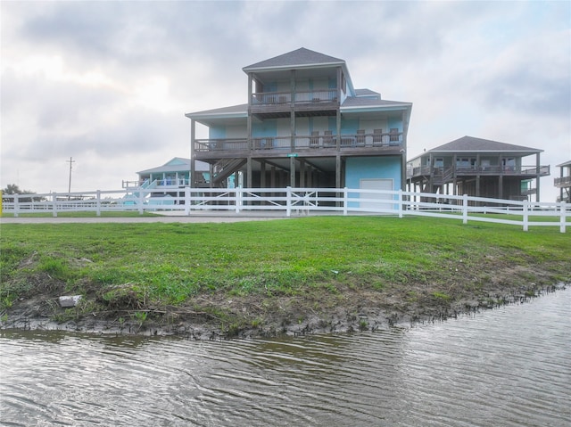 rear view of property featuring a balcony, a water view, and a yard