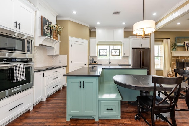 kitchen featuring appliances with stainless steel finishes, white cabinetry, decorative backsplash, and a stone fireplace