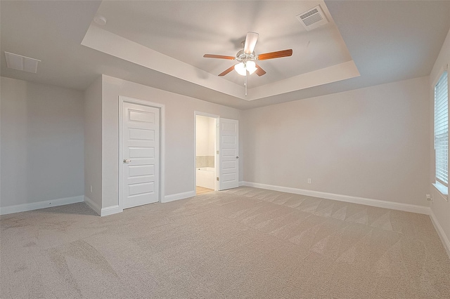 unfurnished bedroom with a tray ceiling, multiple windows, ceiling fan, and light colored carpet