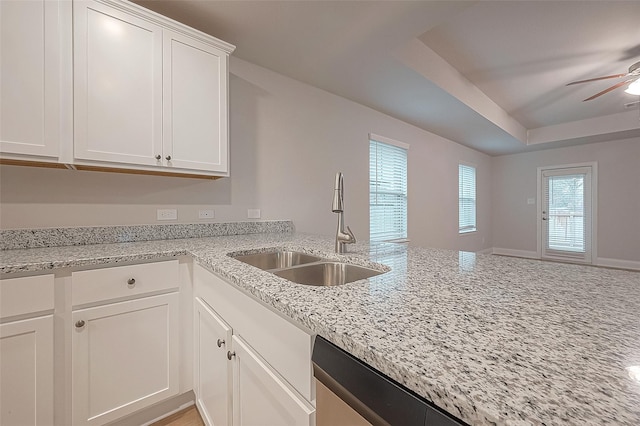 kitchen with light stone counters, white cabinetry, ceiling fan, and sink