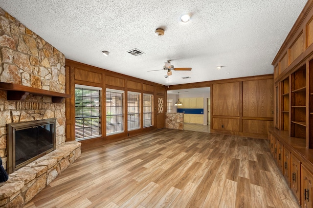 unfurnished living room featuring a fireplace, wood walls, ceiling fan, a textured ceiling, and light wood-type flooring