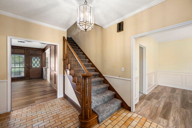 stairs with hardwood / wood-style flooring, crown molding, a notable chandelier, and a textured ceiling