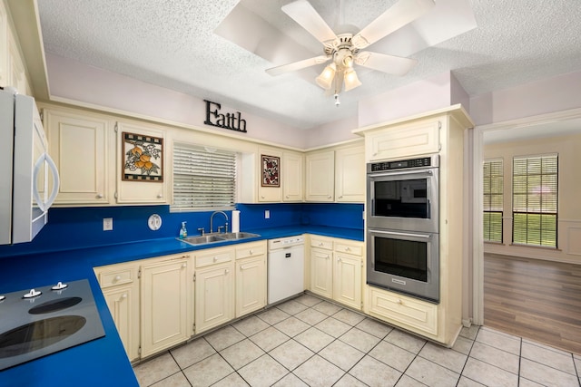 kitchen with sink, light tile patterned floors, white appliances, cream cabinets, and a textured ceiling