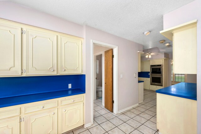 kitchen featuring light tile patterned floors, ceiling fan, cream cabinets, a textured ceiling, and stainless steel double oven