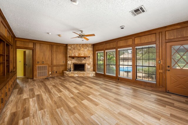 unfurnished living room featuring crown molding, a textured ceiling, a fireplace, and wood walls