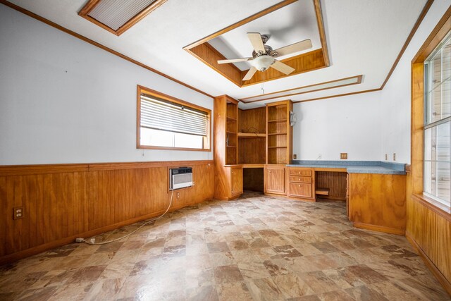 unfurnished office with built in desk, wood walls, ornamental molding, ceiling fan, and a raised ceiling