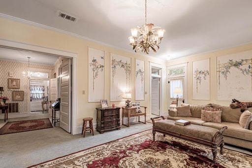 living room with a healthy amount of sunlight, ornamental molding, carpet, and a notable chandelier