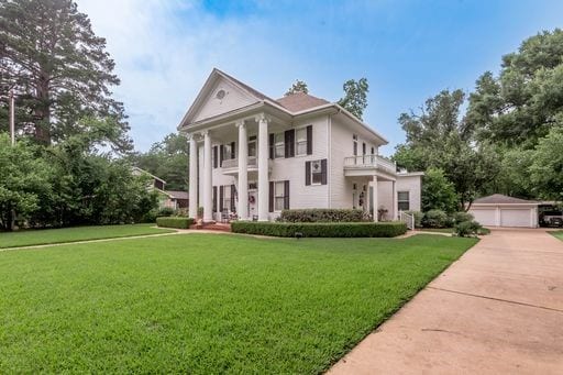 greek revival house featuring a balcony, a front lawn, a garage, and an outdoor structure