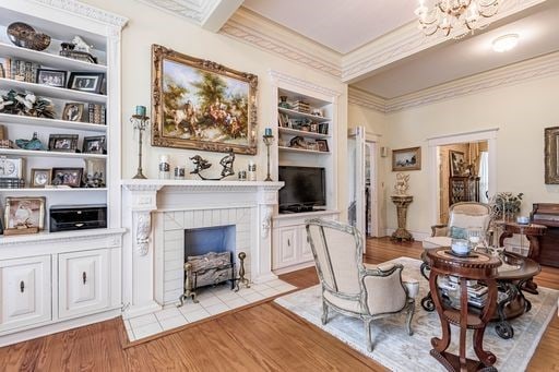 living room featuring ornamental molding, built in features, a tile fireplace, and light hardwood / wood-style flooring