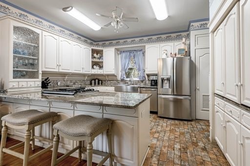 kitchen featuring stainless steel appliances, stone counters, ceiling fan, a breakfast bar area, and white cabinets