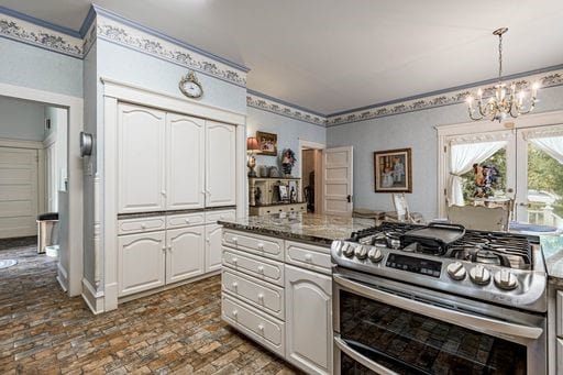 kitchen with stainless steel gas range oven, dark stone counters, white cabinets, decorative light fixtures, and a chandelier