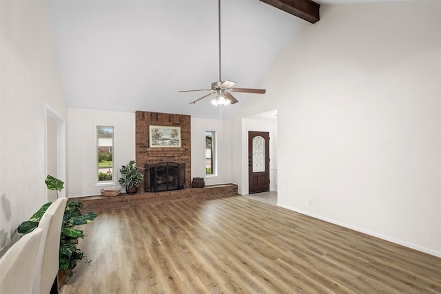 unfurnished living room featuring ceiling fan, high vaulted ceiling, hardwood / wood-style floors, brick wall, and a brick fireplace