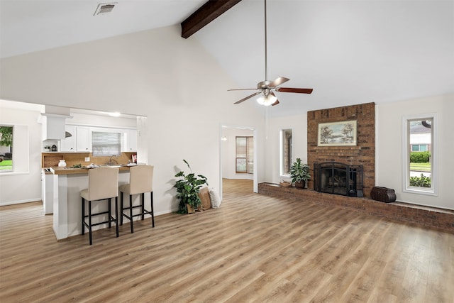 living room featuring a fireplace, high vaulted ceiling, light wood-type flooring, and ceiling fan