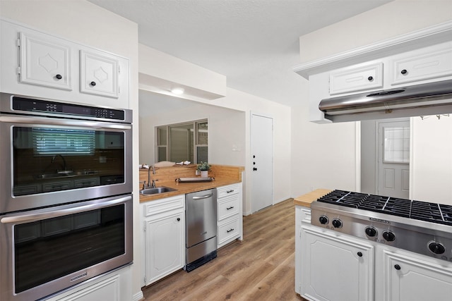 kitchen with stainless steel appliances, white cabinetry, sink, and light hardwood / wood-style flooring