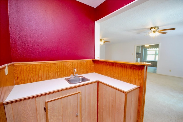 kitchen featuring a ceiling fan, light brown cabinets, light colored carpet, light countertops, and a sink