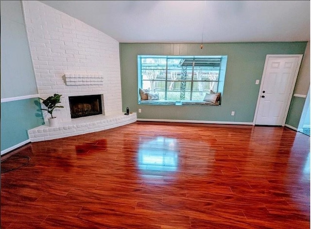 unfurnished living room with a brick fireplace, brick wall, lofted ceiling, and dark wood-type flooring