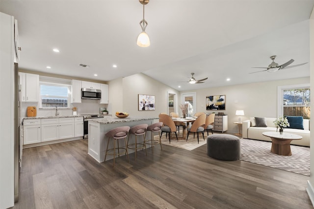 kitchen featuring a breakfast bar area, white cabinetry, hanging light fixtures, stainless steel appliances, and a center island