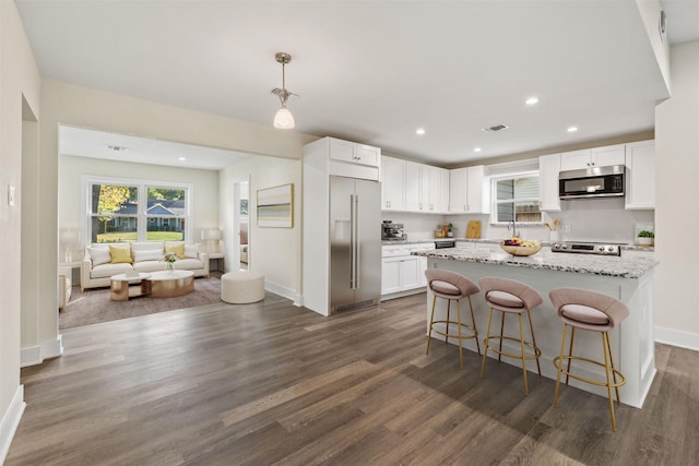 kitchen featuring hanging light fixtures, appliances with stainless steel finishes, white cabinets, and light stone counters