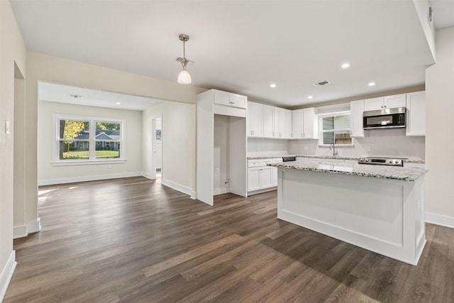 kitchen with light stone counters, a kitchen island, pendant lighting, stainless steel appliances, and white cabinets