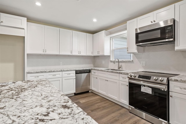 kitchen with sink, appliances with stainless steel finishes, dark hardwood / wood-style flooring, light stone countertops, and white cabinets